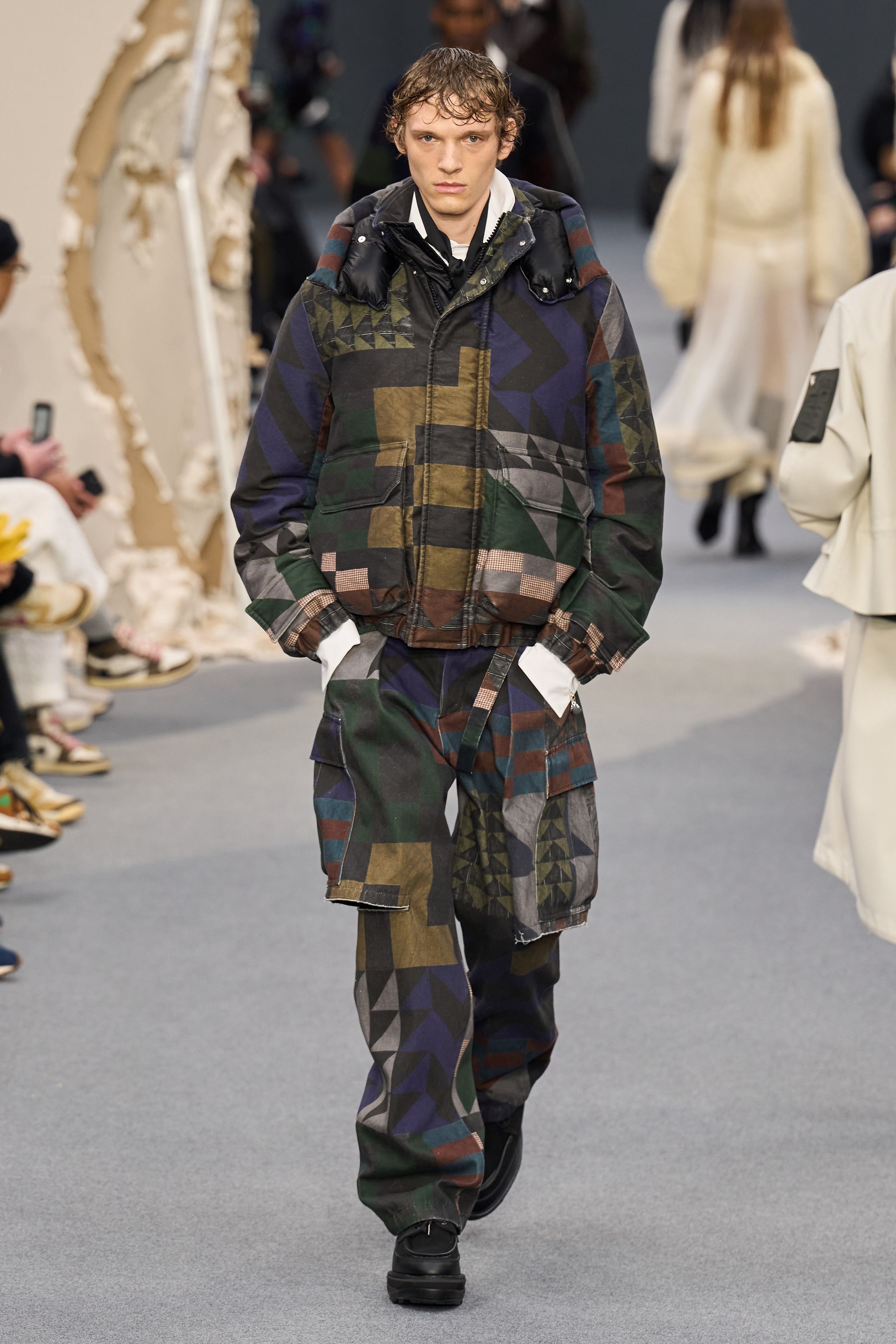 Sacai 2026秋冬再次展示其无可复制的“混合美学”。正装、牛仔、皮草与制服元素被高度结构化地拼接，形成既熟悉又陌生的服装形态。性别边界被进一步模糊，层叠结构制造流动节奏，使行走本身成为设计的一部分。系列在秩序与混乱之间找到平衡，是Sacai 对当代复杂生活状态的持续回应-顽石频道趋势研究